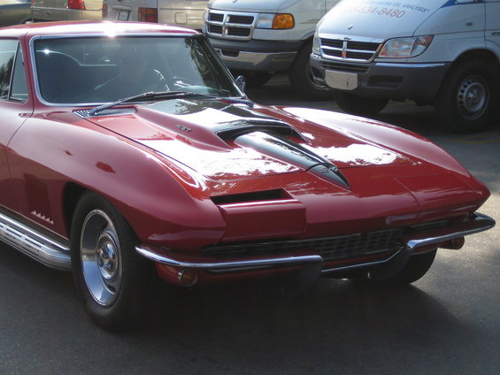 Red 1965 Chevrolet Corvette Sting Ray coupe front view, parked behind vans