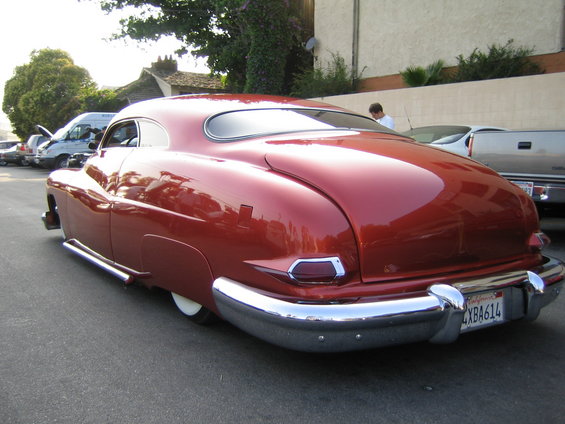 Red 1949 Mercury coupe with chrome bumper and side pipes, seen from rear