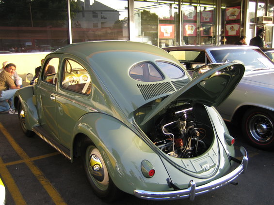 Rear view of a light green Volkswagen Beetle with the engine compartment open, parked next to another car