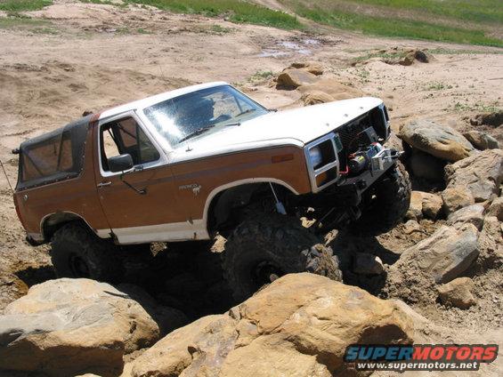 Brown and white Ford Bronco with large tires navigating rocky terrain