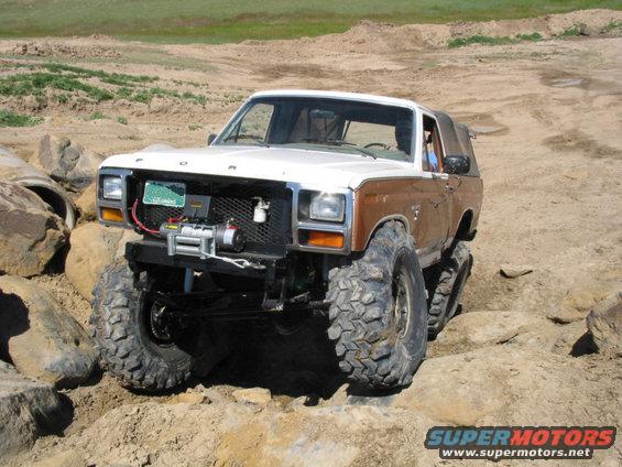 White and brown Ford Bronco with large tires navigating rocky terrain. Winch mounted on front bumper