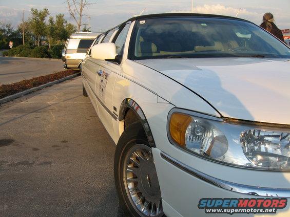 White limousine front quarter view with a white van in the background