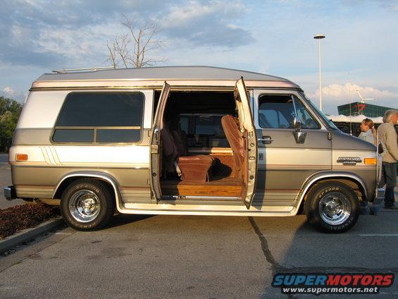 Side view of a two-tone brown and silver conversion van with front doors open, showing brown velour interior
