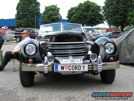 Front view of a black Cord 810/812 convertible with a man sitting in a chair to the left