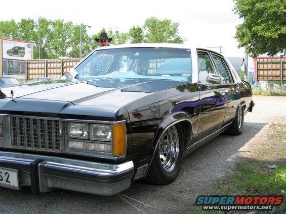 Black sedan with white roof, chrome wheels, and lowered suspension. A person in a hat is visible through the windshield