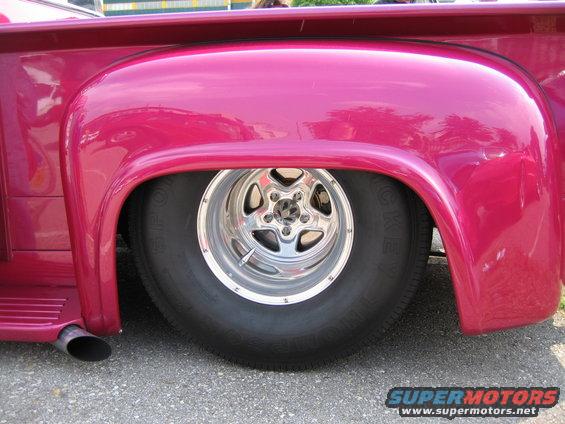 Pink pickup truck rear wheel with chrome five-spoke rim and wide tire, showing part of the fender and exhaust pipe