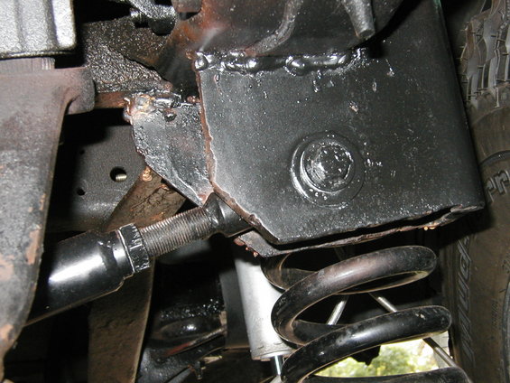 Close-up of black-painted vehicle frame with visible welds, a shock absorber, and a coil spring
