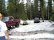 1989 Ford Bronco - Two vehicles are stuck in the snow in a wooded area, with one attempting to tow the other out.