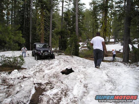 Dark blue Jeep Wrangler with winch on snowy mountain trail, two men nearby