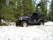 1989 Ford Bronco - A dark blue Jeep Wrangler navigates through a snowy forest trail.