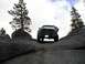 1989 Ford Bronco - A pickup truck navigates a challenging rocky path in a mountainous, wooded area under a cloudy sky.