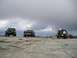 1989 Ford Bronco - Three off-road vehicles are parked on a rocky surface with a cloudy sky overhead.