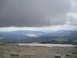 1989 Ford Bronco - A vast mountain vista unfolds, a lake among forested hills under a dramatic, overcast sky.