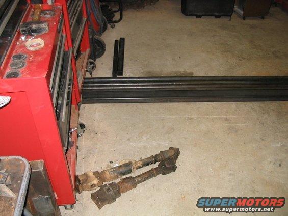 Two driveshafts and metal stock next to a red toolbox