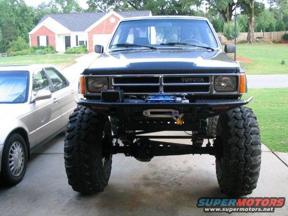 Lifted Toyota pickup truck front view with winch and large tires. Visible "TOYOTA" badge
