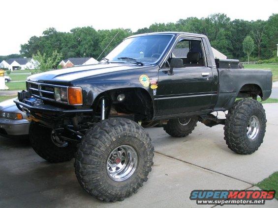 Lifted black Toyota pickup truck with large off-road tires, custom bumper, and toolbox