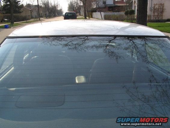 Rear window and roofline of a car, with another car visible in the distance on a residential street