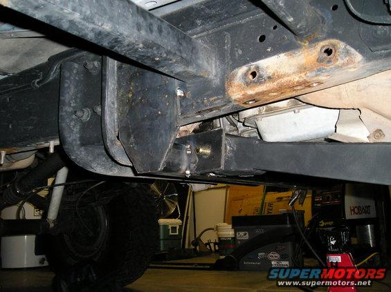 Underside view of vehicle frame with suspension parts and a tire visible. Some rust on frame