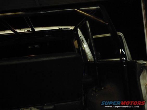 Roll cage installed inside a vehicle. The cage covers the rear passenger area and extends to the roof