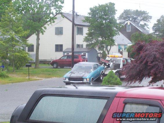 Blue coupe with a black hood on a tow truck, front view