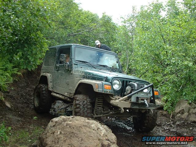 Green 2000 Jeep TJ off-roading on a muddy trail with large tires and a winch