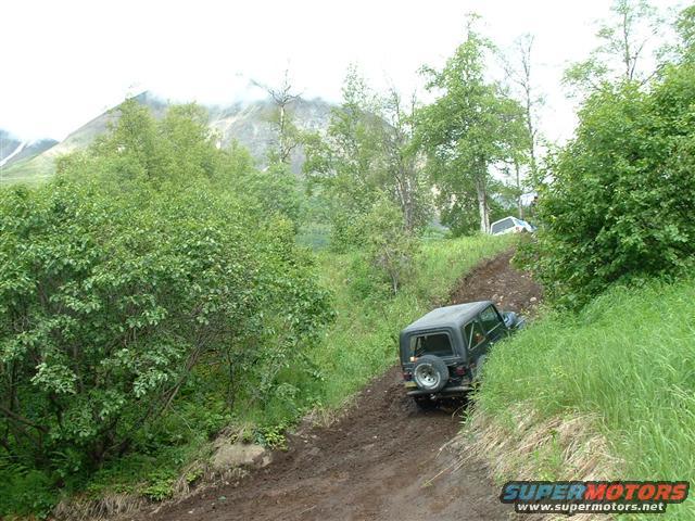 Black Jeep TJ driving on a muddy hill with another white SUV in the background