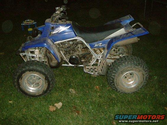 2004 Suzuki QUADRUNNER 250/LT250 ATV parked on grass. Visible text includes 'QUADRUNNER 250' and 'SUPERMOTORS.NET'