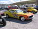 1972 Ford Mustang - A yellow muscle car with flame graphics and a supercharger is parked at an outdoor event, with other vehicles and trailers visible.