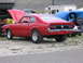 1972 Ford Mustang - A red coupe with its hood open is parked on a gravel lot next to other vehicles and RVs.