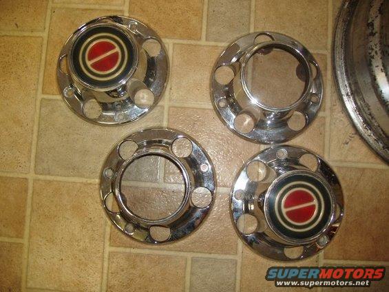 Four chrome hubcaps with red and black center emblems, laid out on a tiled floor