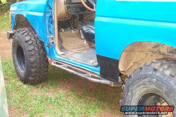 Side view of a blue SUV with door open, showing interior and large off-road tires. Custom metal steps are visible below the door