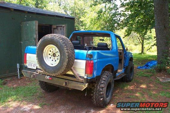 1987 Ford Bronco, blue, with spare tire mounted on rear bumper, parked outside a shed