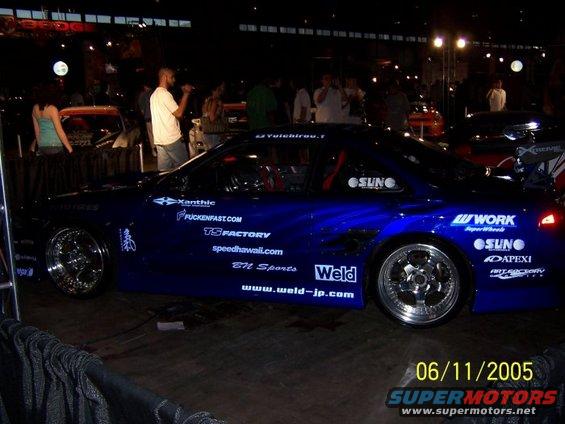 Blue sports car with many sponsor decals, chrome rims, and a large rear spoiler. Date stamp shows 06/11/2005