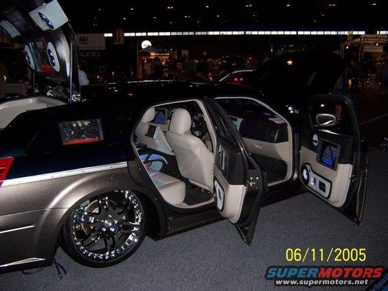 Customized sedan with open doors, large rims, and interior screens. Date stamp shows 06/11/2005