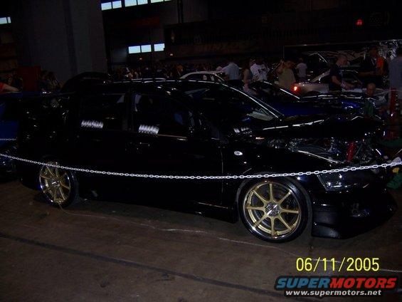black sedan with gold rims, hood open, at a car show