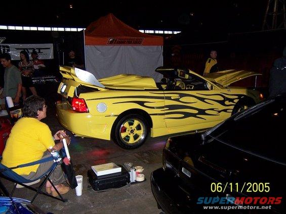 Yellow convertible with black flame decals and a large rear spoiler, parked next to a black car. Date stamp reads 06/11/2005