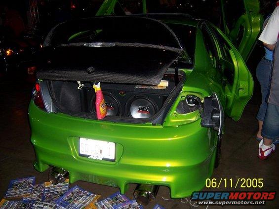Green sedan with custom body kit, aftermarket spoiler, and lambo doors, rear view showing trunk with subwoofers and a spray bottle