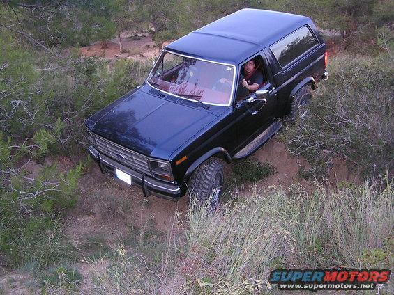 Black Ford Bronco driving on a dirt path with brush on either side. Driver is visible