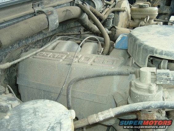 Dusty engine bay with hoses and engine components visible