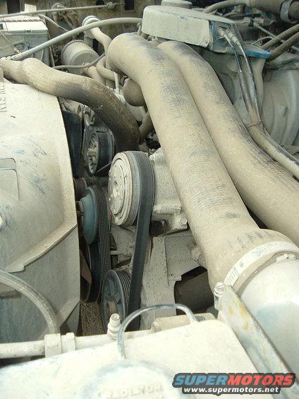 Engine bay showing belts, pulleys, and large hoses. Some dust covers engine components