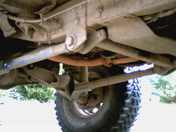 Underside view of a lifted vehicle's suspension and exhaust system, showing off-road tires