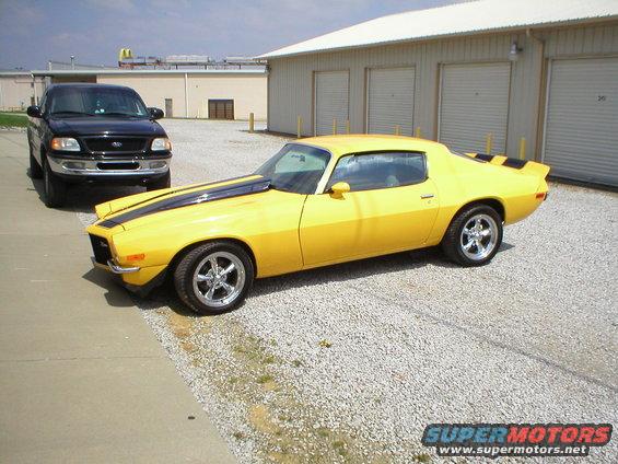 yellow muscle car with black stripes parked next to a black pickup truck