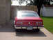 1974 Ford Maverick - The rear of a red sedan is parked in a driveway next to a stone wall and wooden fence.