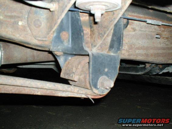 Underside view of rusty vehicle suspension components, showing a bracket and bushings