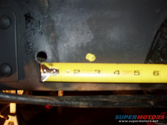 Yellow tape measure showing approximately 3.5 inches against a dark, textured surface with a hole
