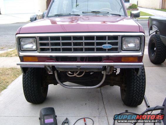 1985 Ford Bronco II front view, showing grille, headlights, and custom bumper. Another vehicle is partially visible to the right