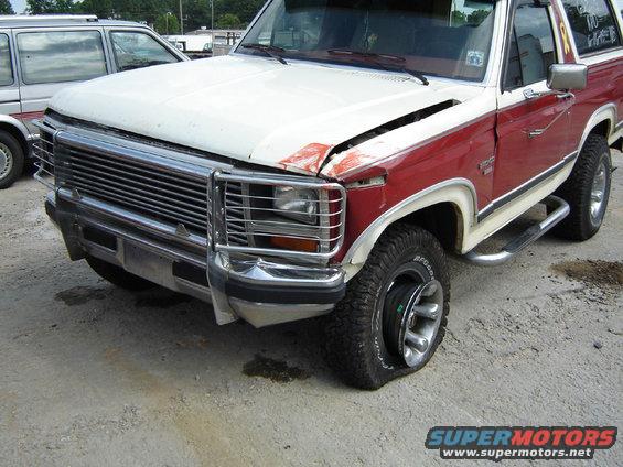Red and white Ford Bronco with a flat front tire, parked next to a silver van