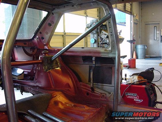 Car interior stripped down with a roll cage installed. Welding equipment is visible to the right