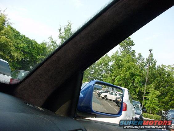 Cars in a parking lot reflected in a blue side mirror, with trees and a lamppost in the background