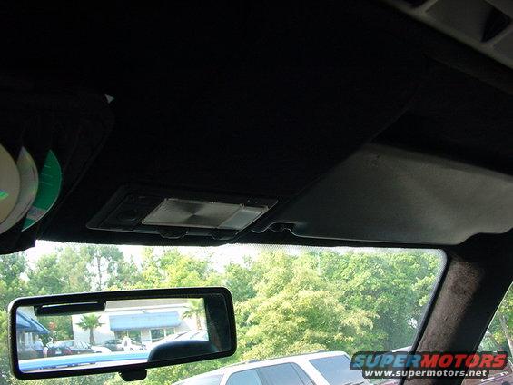 Interior view of car with CDs on visor and rearview mirror showing trees and buildings